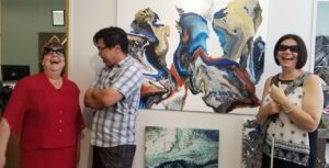 A man and two women standing in front of a large acrylic painting of a dragon