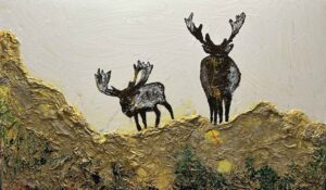 "Artwork titled 'Trek of the Caribou' depicting a caribou with a brown and white coat and large antlers standing in a rugged, mountainous landscape. The background features dark, rocky hills and a misty blue sky, with thick, textured paint adding a three-dimensional feel to the piece."