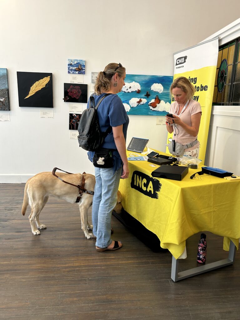 a woman with her seeing eyed dog standing at the CNIB booth at my my migration exhibit.