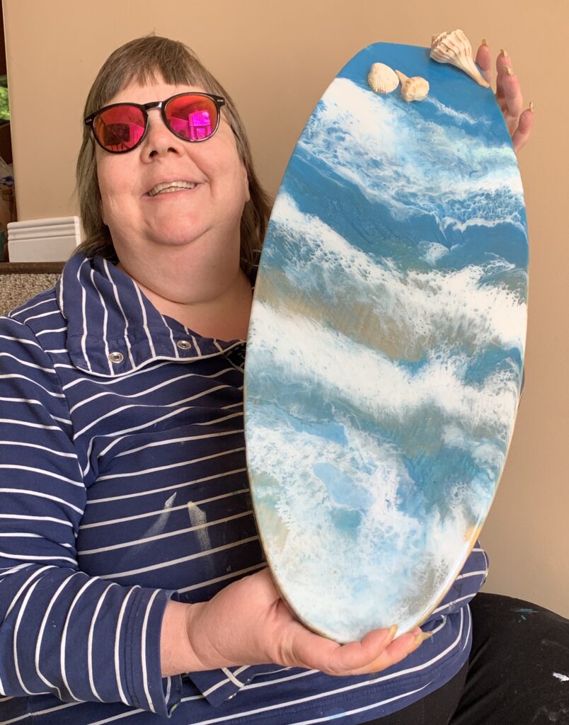 Lynda holding the paddle board she created for the Cobourg BIA Ukraine fundraiser. It was on display for the summer of 2023 in a business front window. and then put up for auction.