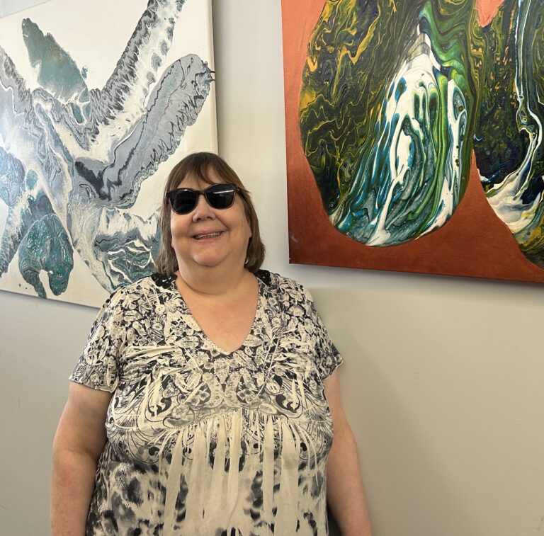 Lynda standing in front two art pieces at the Cobourg Gallery.